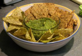 Bowl of avocado dip surrounded by chips.