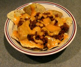 A bowl of chili, chips, and cheese.