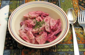 A bowl of pink potato salad garnished with parsley flakes.
