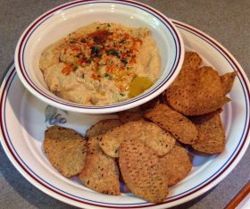 A bowl hummus garnished with oil, paprika, and parsley flakes.